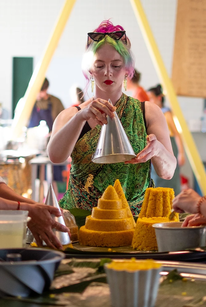 Three women prepare cone-shaped yellow rice dishes together during a Culinary Roots gathering.