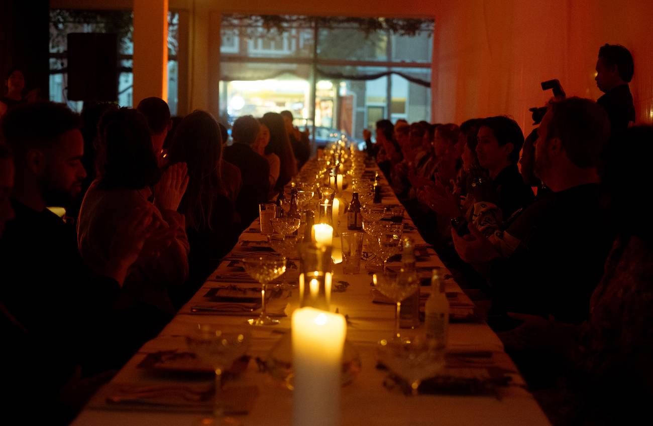 A dimly lit dinner setting with a long table, adorned with candles and elegant glassware