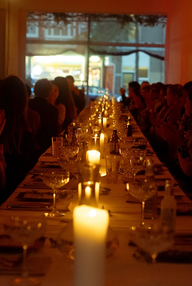 A dimly lit dinner setting with a long table, adorned with candles and elegant glassware