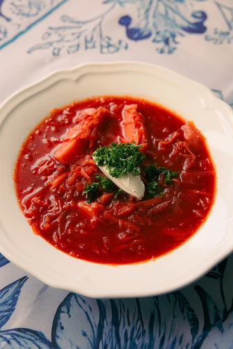 A white bowl of vibrant red borscht with beet chunks, garnished with a dollop of sour cream