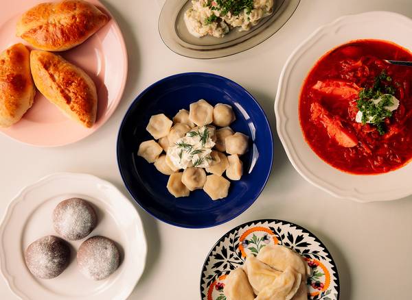 Dishes on colorful plates: dumplings with dill, borscht with herbs and cream, pastries and salad.