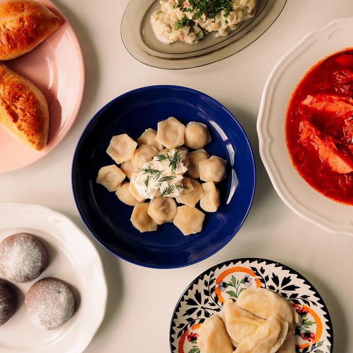 Dishes on colorful plates: dumplings with dill, borscht with herbs and cream, pastries and salad.