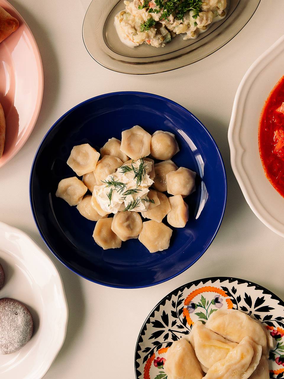 Dishes on colorful plates: dumplings with dill, borscht with herbs and cream, pastries and salad.