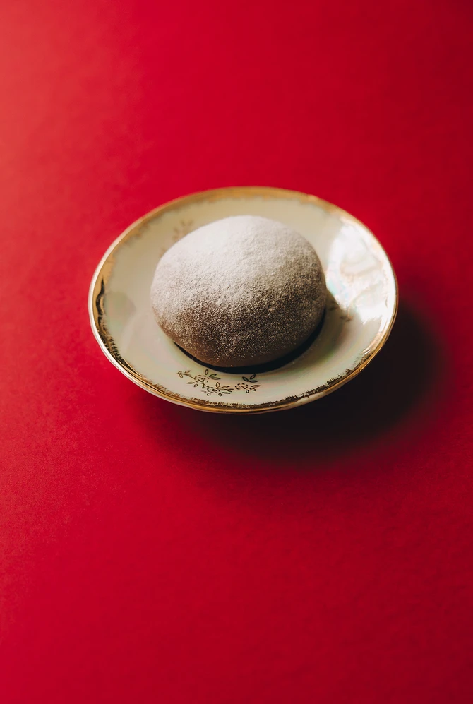 A single powdered kartoshka sits on an ornate plate against a vibrant red background