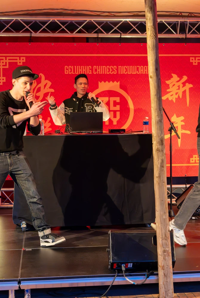 Three performers on stage, in front of a red banner with Chinese New Year greetings.