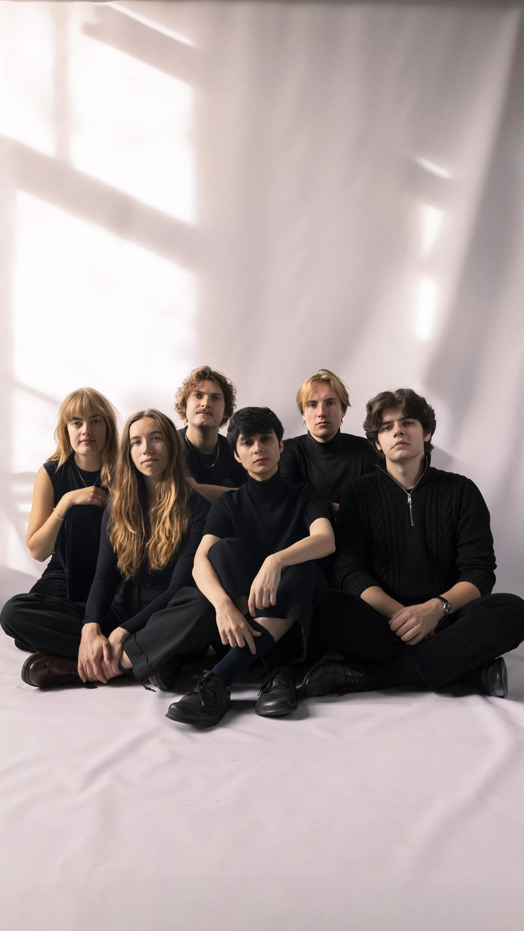 Six members of Mahala dressed in black sit together against a backdrop.