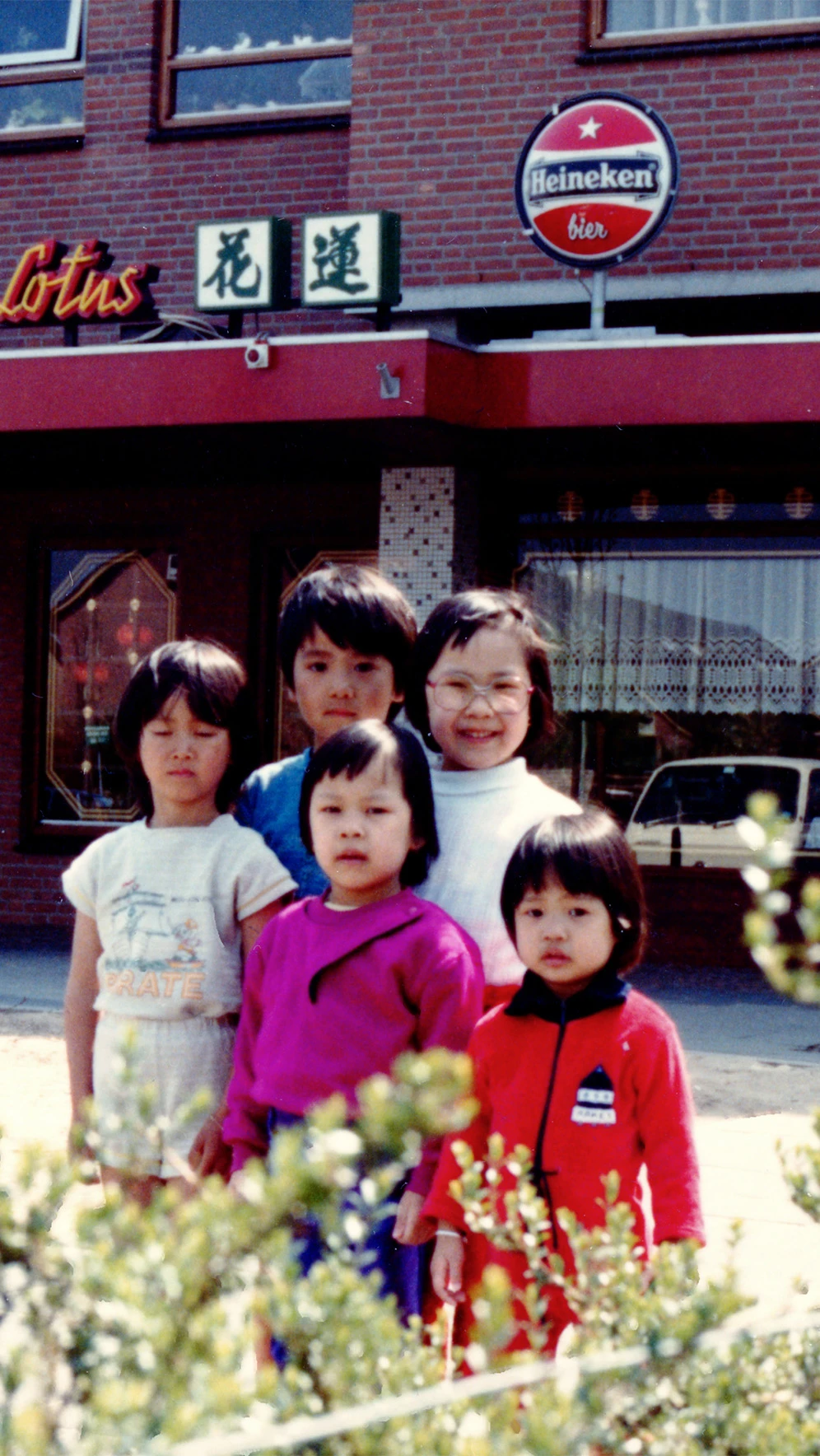 A group of children stand happily in front of a Chinese restaurant named "Lotus."