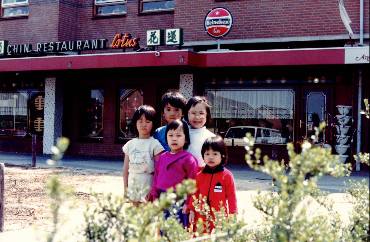 A group of children stand happily in front of a Chinese restaurant named "Lotus."
