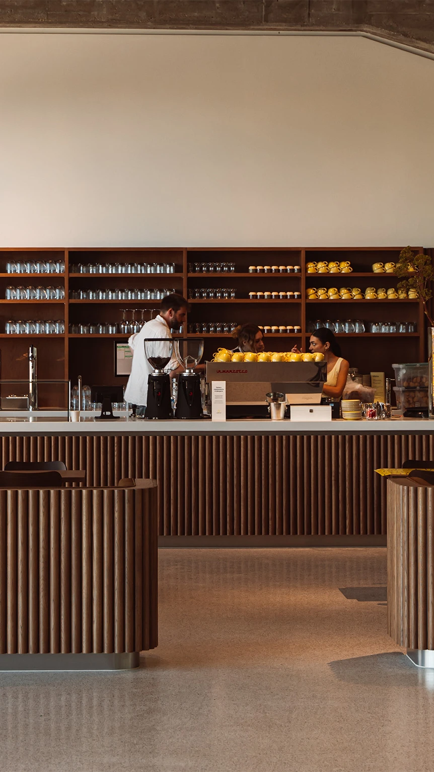 A cafe with a lot of wooden elements. Behind the coffee bar are employees talking to each other.