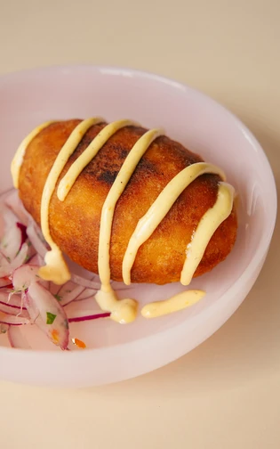 Goudbruine aardappelkroket met saus en plakjes rode ui op een bord.