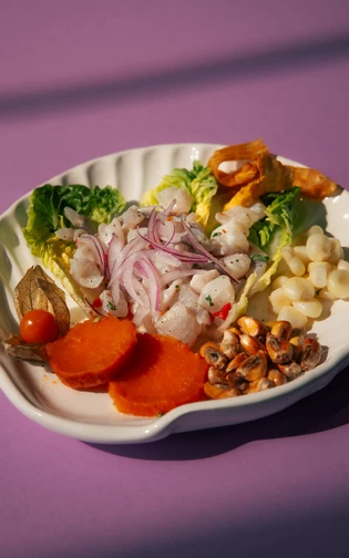 Bord met ceviche van vis, rode ui, sla, zoete aardappel, maïs en schelpdieren.