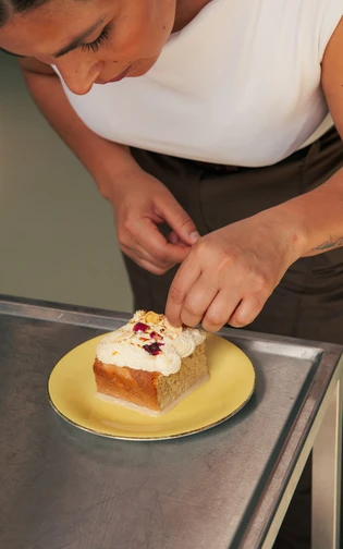 Een vrouw werkt aan de garnering van een stuk taart op een geel bord