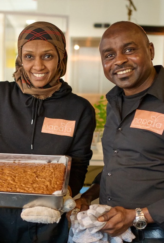 Ranya and Abdelrahman smiling in the kitchen while holding a freshly baked dish from Napata.