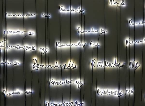 An illuminated installation featuring the words ‘Remember Me’ written repeatedly in different handwr