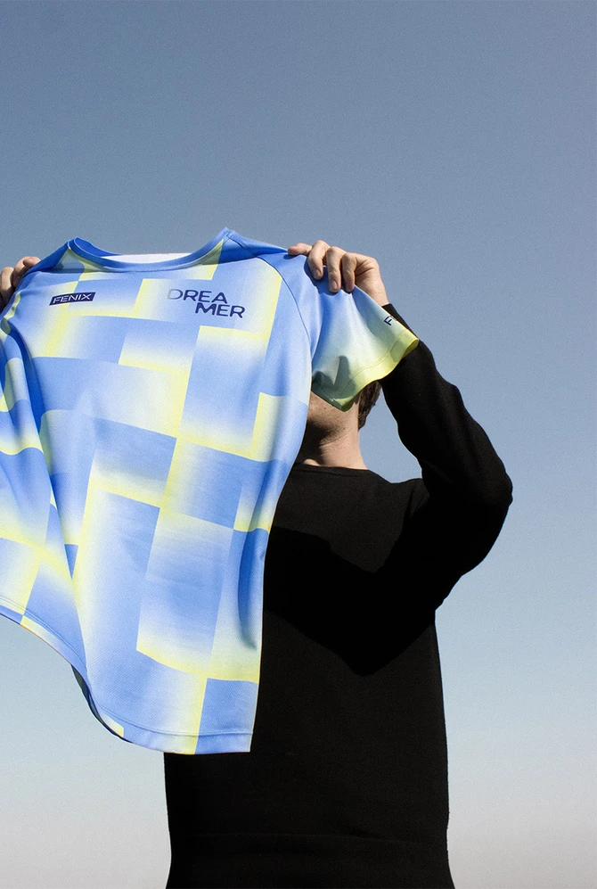 een persoon houd een hardloopshirt in de lucht, afgetekend tegen de blauwe lucht