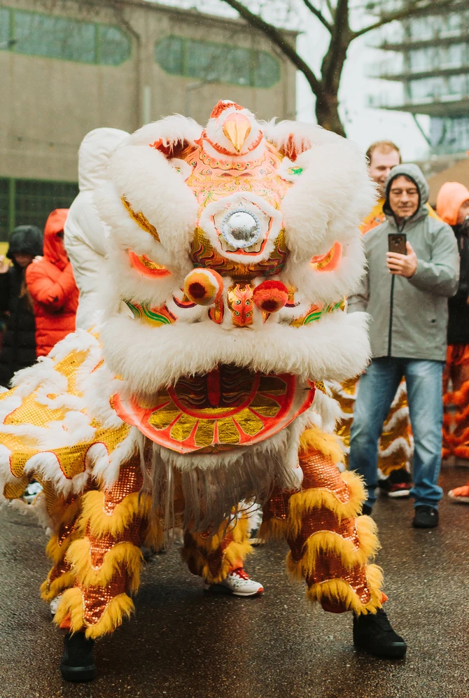 A vibrant lion dance with an orange and white costume dazzles a smiling crowd