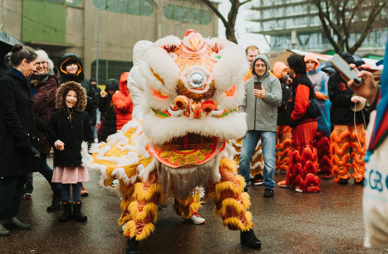 A vibrant lion dance with an orange and white costume dazzles a smiling crowd