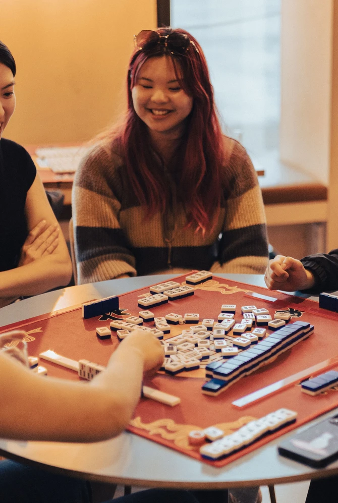 A group of five people sits around a round table playing mahjong