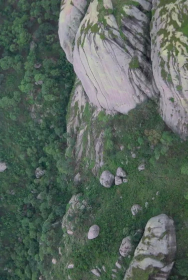 still from the film: Aerial view of lush green mountains with large, rugged boulders scattered