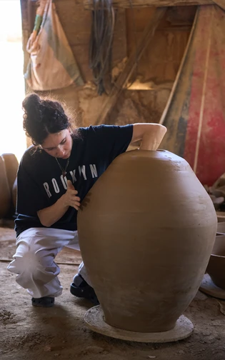 A ceramic artist shaping a large clay vessel by hand in a rustic workshop.