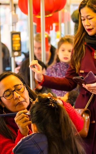 A woman applies face paint to a child's face inside a bus decorated with red lantern