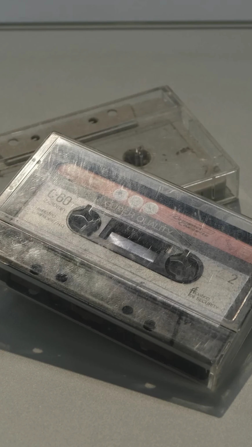 twee cassettebandjes met rode opdruk liggen op een grijze ondergrond, als in een museum