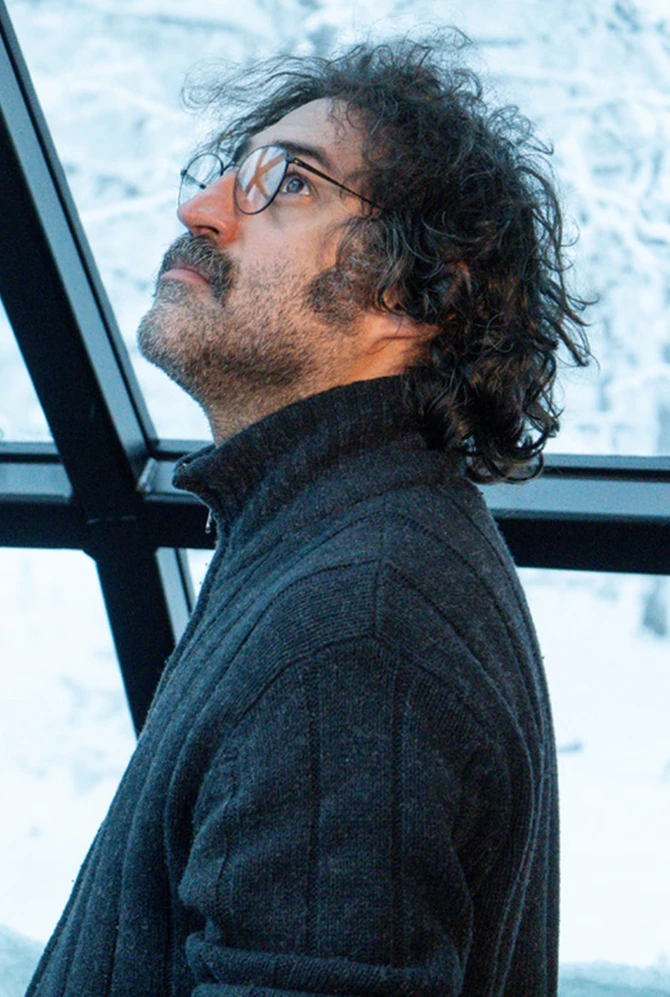 A man looks up inside a room with large windows, with a snowy landscape in the background.