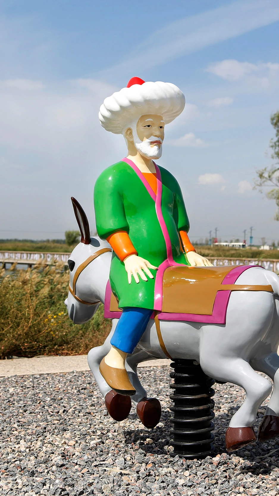 Beeld van Molla Nasreddin op een ezel, vormgegeven als speeltoestel in een parklandschap.