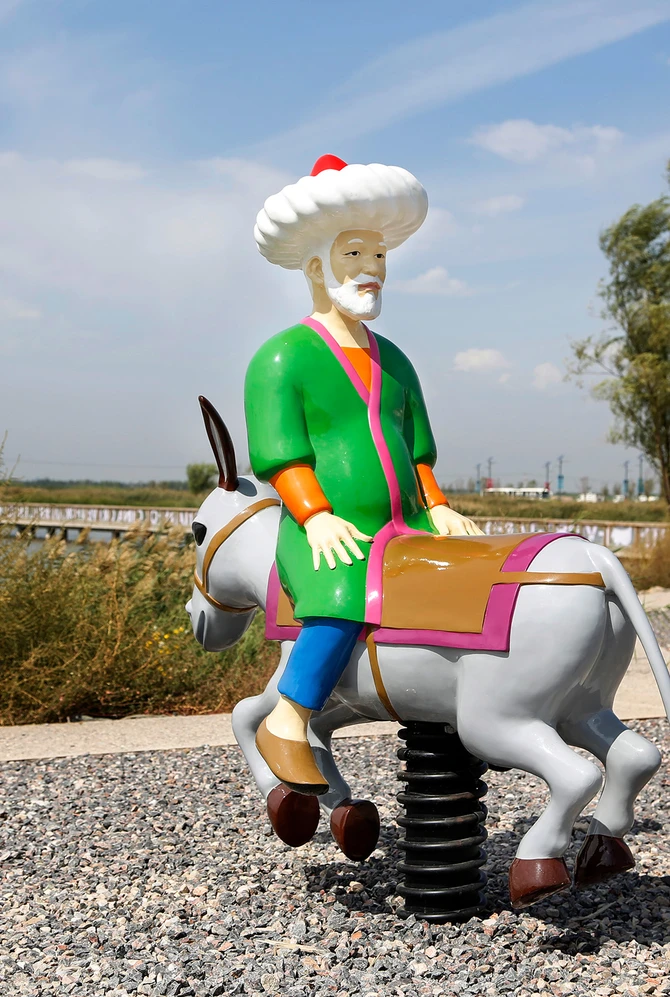 Beeld van Molla Nasreddin op een ezel, vormgegeven als speeltoestel in een parklandschap.