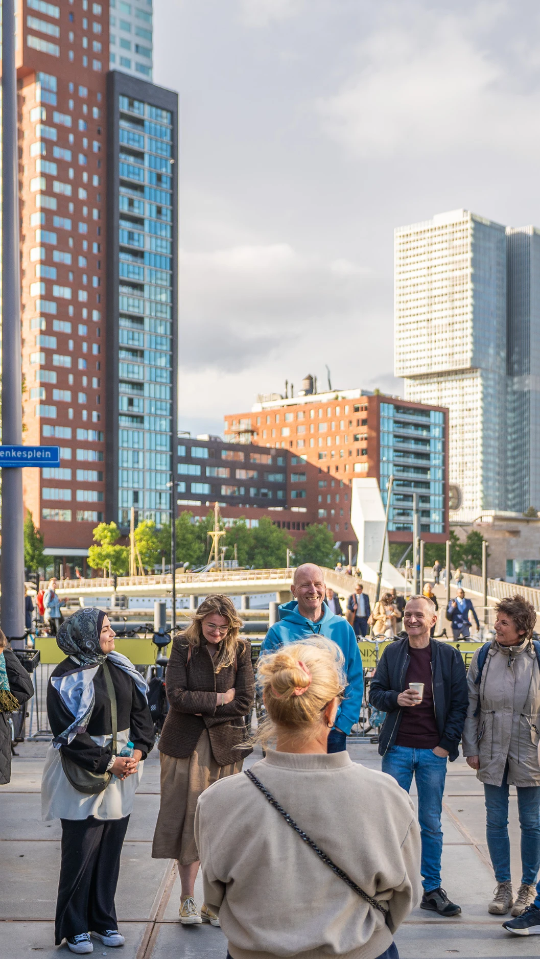 A diverse group of people stands in a circle on a city street, engaged and smiling. Tall buildings a