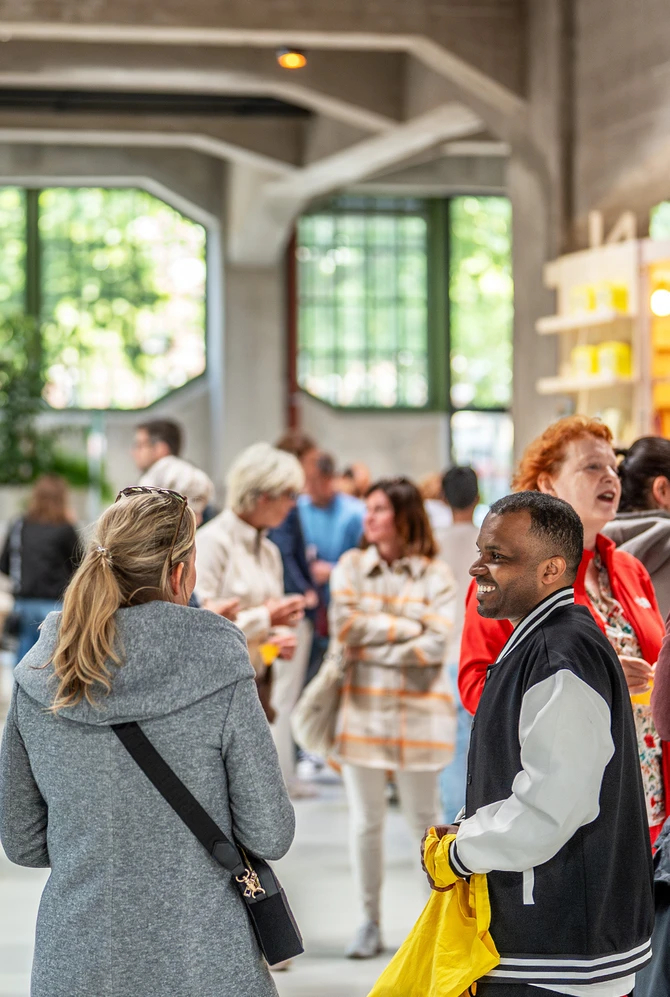 A group of people engaging in conversation at a bright, spacious indoor event with large windows and