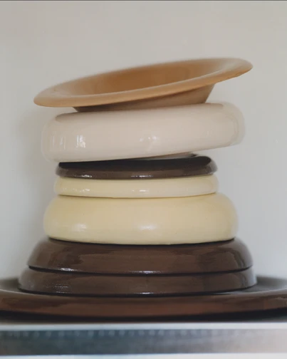 A stack of glazed ceramic plates and bowls in earthy brown, cream and yellow tones.
