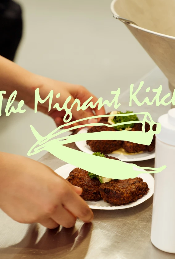 A staff member serves dishes in a kitchen, overlaid with The Migrant Kitchen logo.