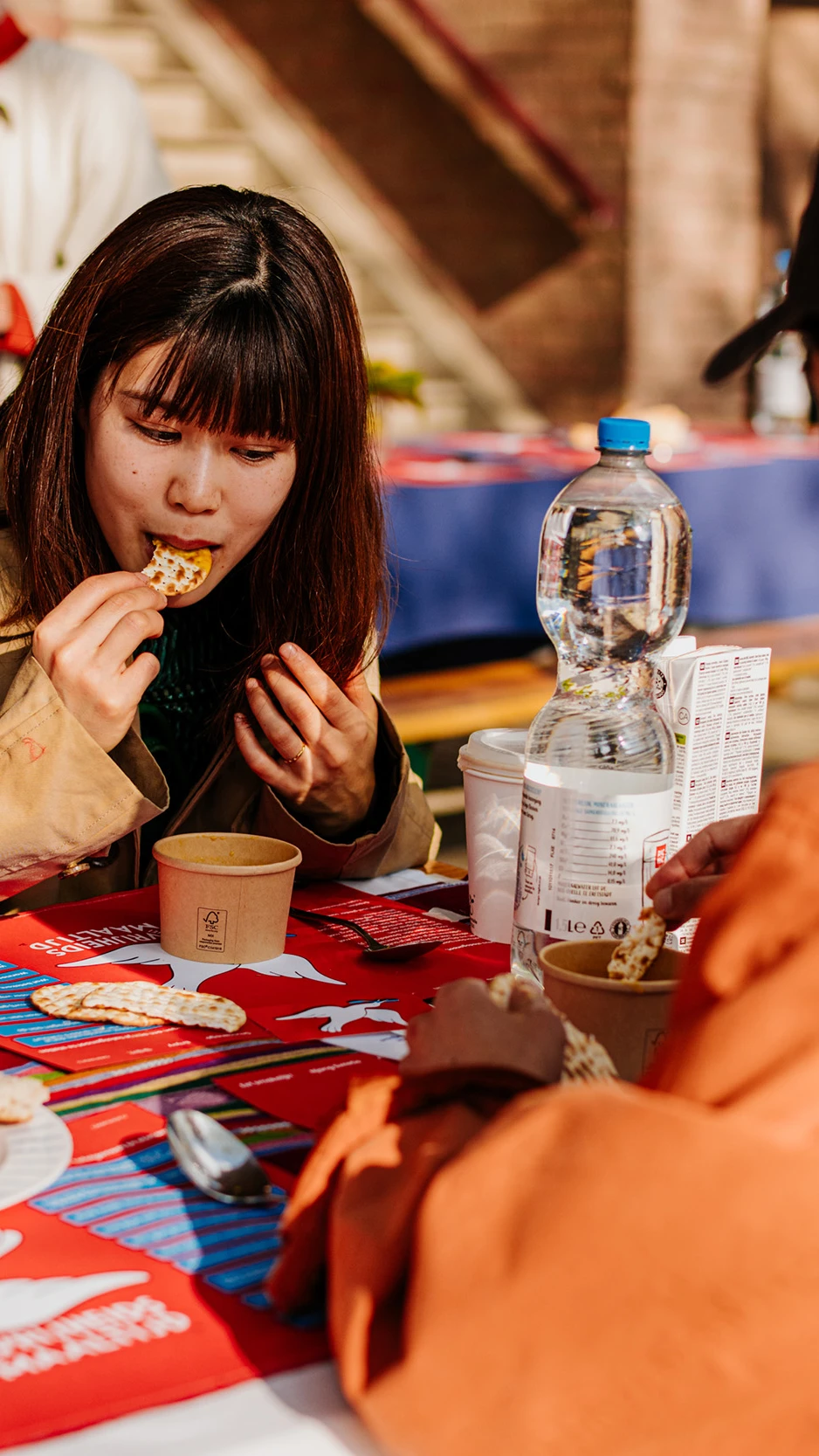 Two people sit at an outdoor table enjoying a casual meal with crackers and bread.