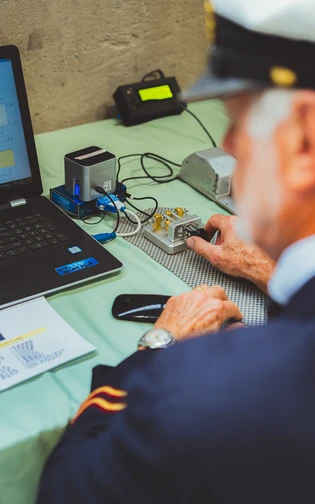 a maritime uniform operates a Morse code key connected to a laptop.