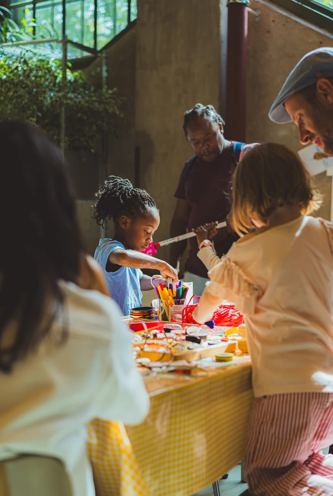 Kinderen en volwassenen knutselen aan een tafel met een geel tafelkleed.