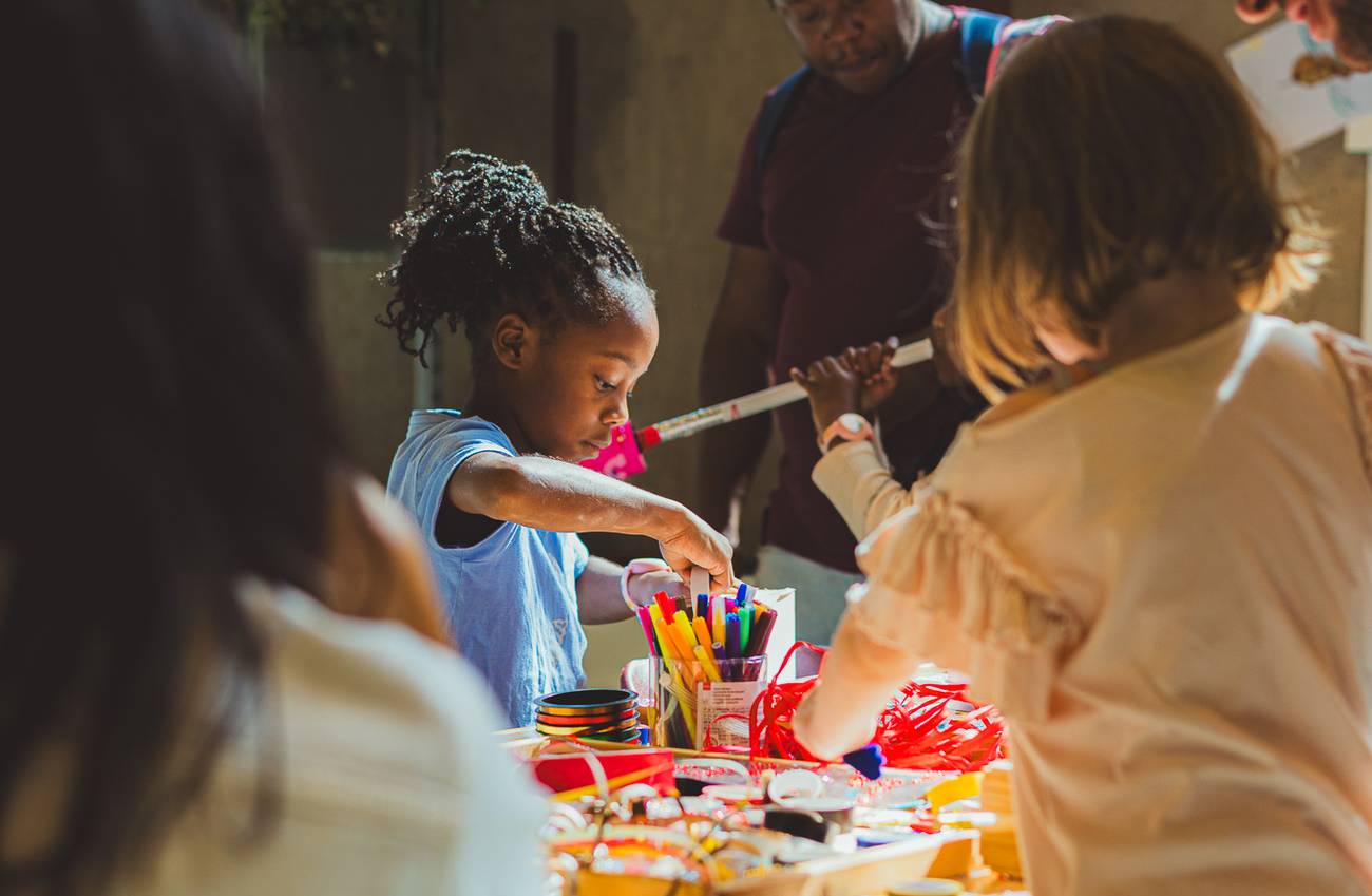Kinderen en volwassenen knutselen aan een tafel met een geel tafelkleed.