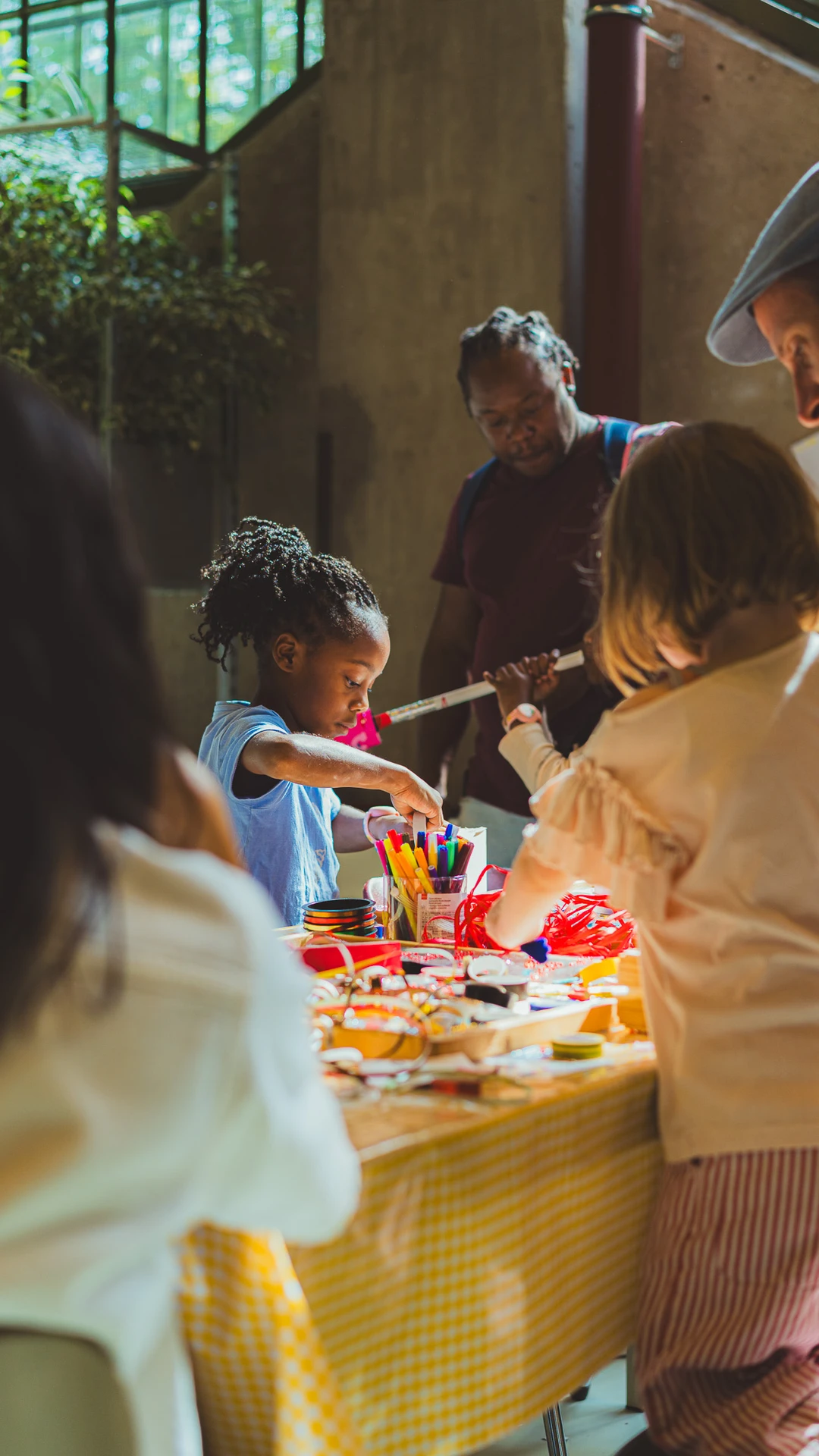 Kinderen en volwassenen knutselen aan een tafel met een geel tafelkleed.