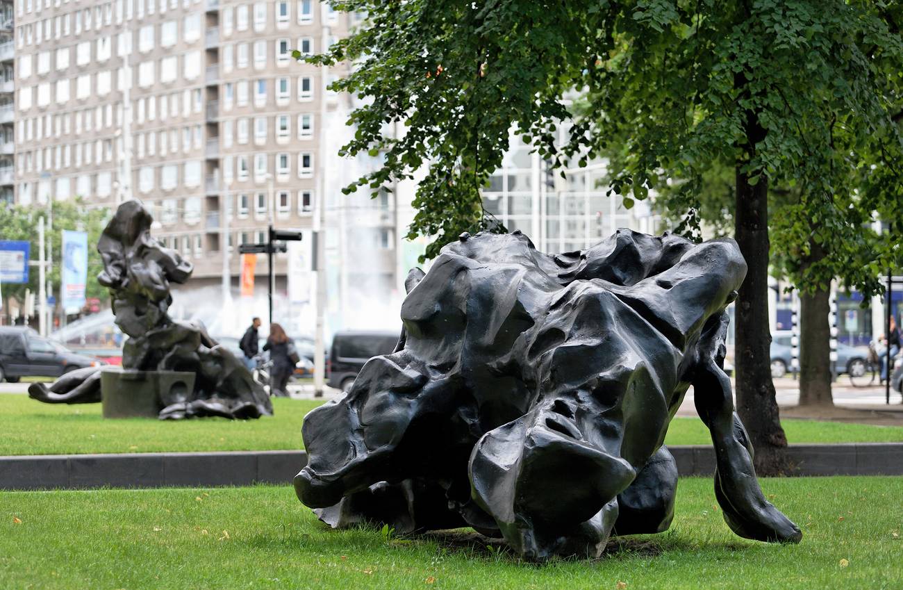 Abstract black bronze sculptures are displayed on a grassy area in an urban setting.