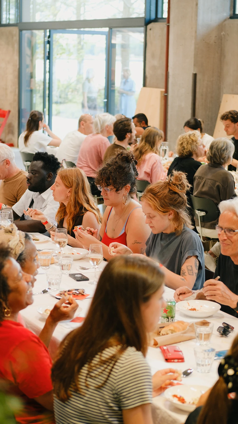 twee lange gedekte tafels waar een divers gezelschap aan zit te eten, de sfeer is zomers