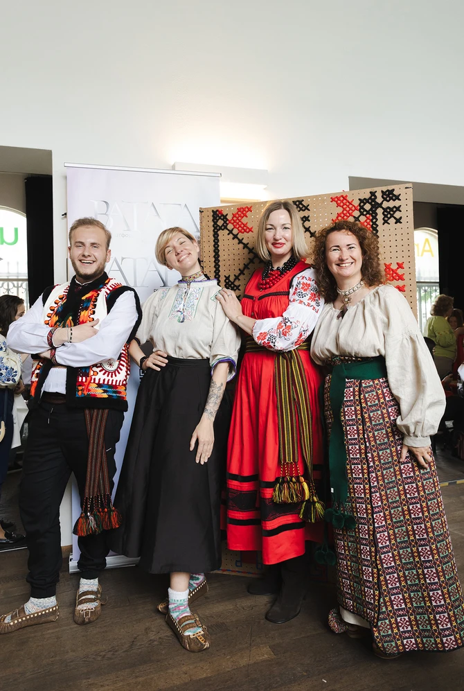 Four people in traditional Eastern European clothing smile joyfully.