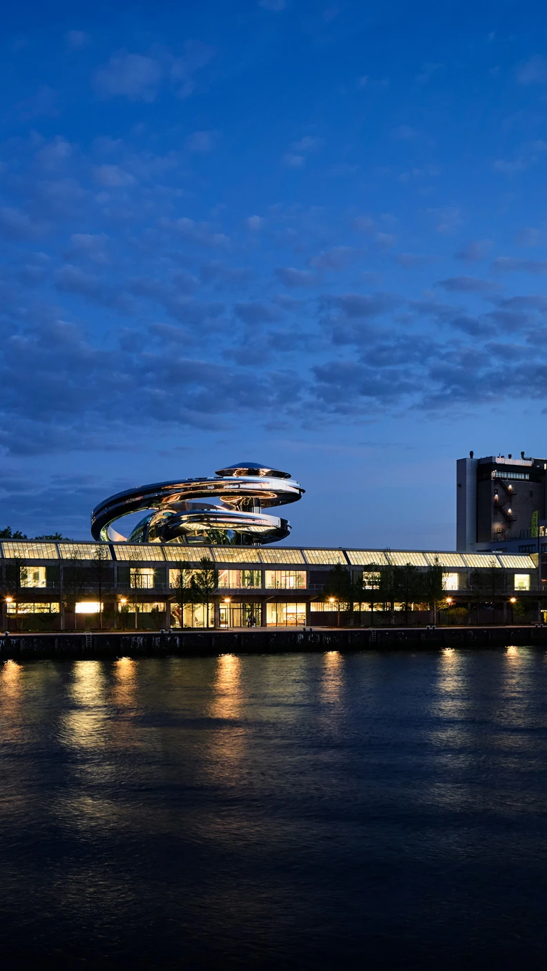 Fenix museum gezien vanaf de overkant van het water. Het is donker en de lichten binnen staan aan.
