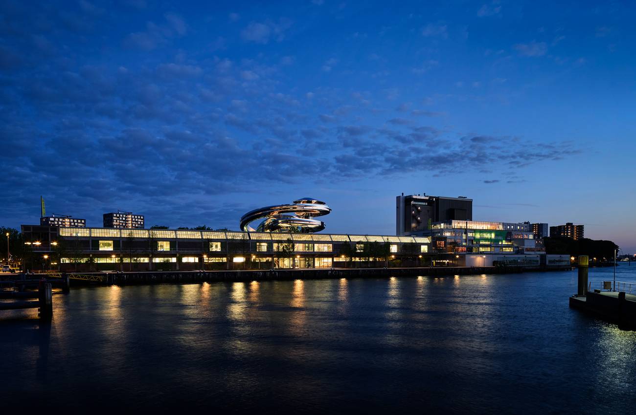 Fenix museum gezien vanaf de overkant van het water. Het is donker en de lichten binnen staan aan.