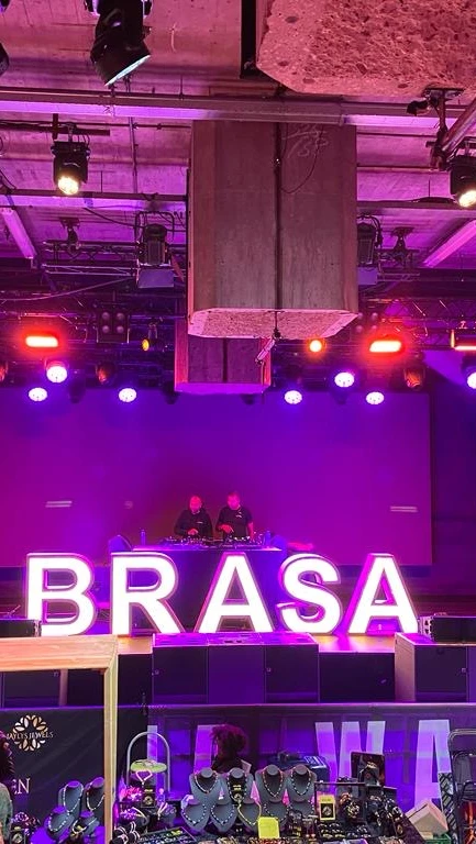 Een ruimte waar Brasadag gevierd wordt: een markt, een dj, en met grote verlichte neonletters 'brasa