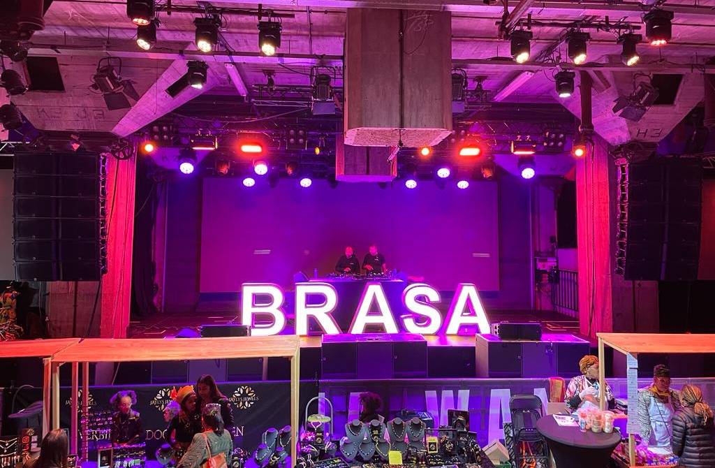 Een ruimte waar Brasadag gevierd wordt: een markt, een dj, en met grote verlichte neonletters 'brasa