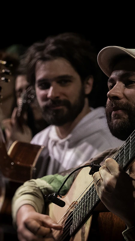 Three men playing guitars sit closely together, focused and relaxed.