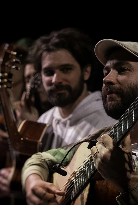 Three men playing guitars sit closely together, focused and relaxed.