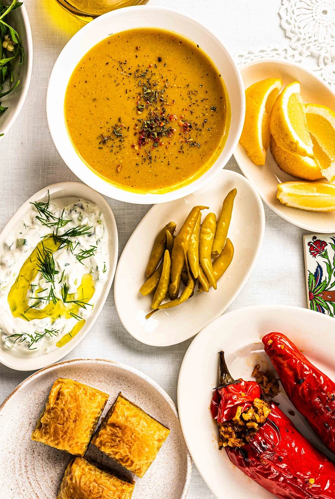 A top view of a table filled with various dishes, including stuffed red peppers, lentil soup, a sala
