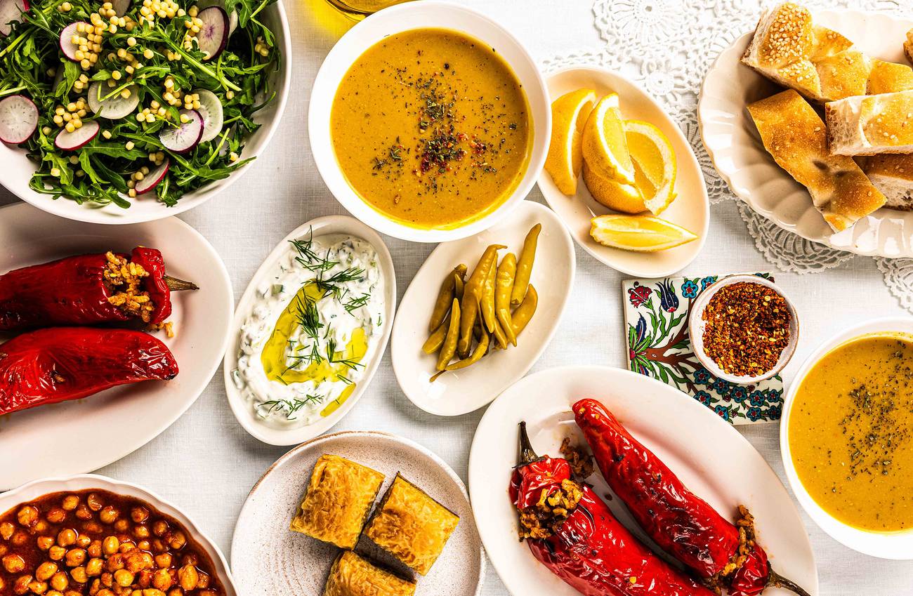 A top view of a table filled with various dishes, including stuffed red peppers, lentil soup, a sala
