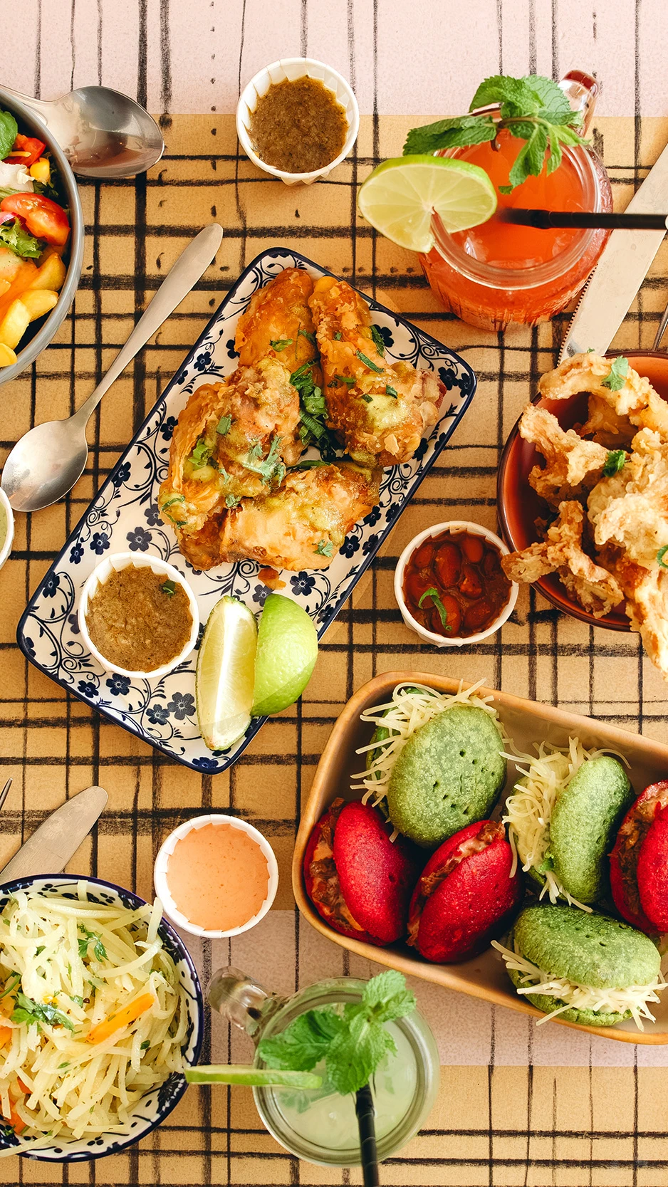 Gedekte tafel met sandwiches, salades, desserts en drankjes, kleurrijk gebak en diverse sauzen.